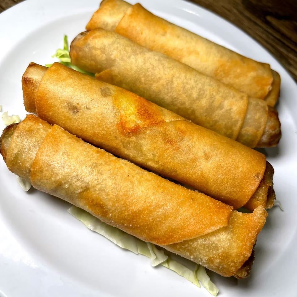 Four golden-brown, crispy Hawaiian spring rolls on a white plate with shredded lettuce.
